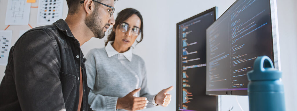 Hispanic man and woman data scientists work on programs together across multiple monitors with data and code