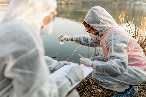 two researchers in personal protective equipment take samples from a pond