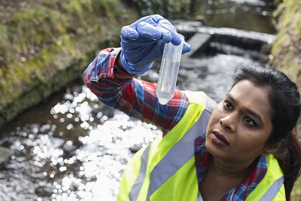 a female scientist checks for signs of microplastics or pollutants in the water sample she has just collected